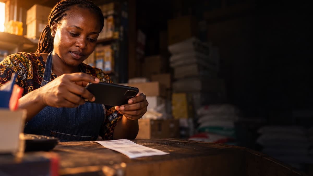 A shop owner photographs a supplier receipt on her counter